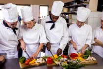 Gruppo di chef che tagliano verdure in cucina — Foto stock