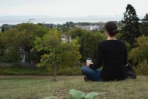 Vista trasera de la mujer tomando café mientras está sentado en una colina - foto de stock