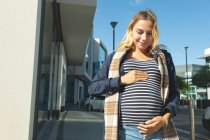 Беременная женщина трогает свой живот в городе в солнечный день — стоковое фото