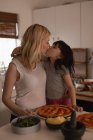 Madre che bacia sua figlia mentre prepara il cibo in cucina a casa — Foto stock