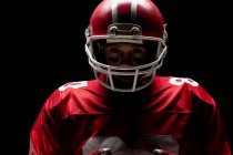 American football player standing with rugby helmet against black background — Stock Photo