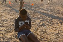 Niño usando el teléfono móvil en el suelo en un día soleado - foto de stock