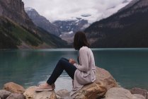 Vista laterale della donna seduta sulla roccia vicino al lago — Foto stock