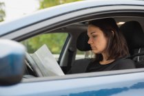 Beautiful woman looking at map in the car — Stock Photo
