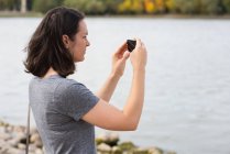 Bella donna cliccando foto con macchina fotografica vicino riva del fiume — Foto stock