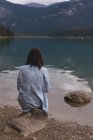 Вид ззаду жінки, що сидить біля берега озера — стокове фото