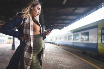 Вид збоку вагітній жінці за допомогою мобільного телефону на залізничному вокзалі — стокове фото