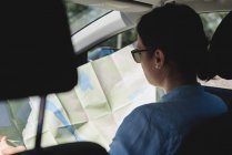 Vista trasera de la mujer mirando el mapa en un coche - foto de stock