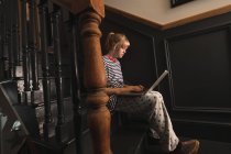 Vista lateral da mulher usando laptop nas escadas em casa — Fotografia de Stock