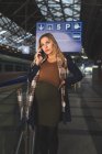 Беременная женщина разговаривает по мобильному телефону на вокзале — стоковое фото