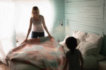 Mère et fille plaçant la couverture sur le lit dans la chambre à coucher à la maison — Photo de stock
