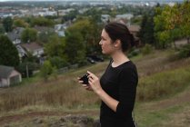 Femme réfléchie tenant une caméra sur une colline — Photo de stock