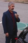 Зрелый бизнесмен разговаривает по мобильному телефону во время зарядки электромобиля — стоковое фото