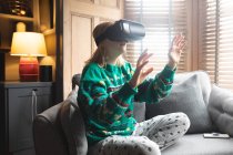 Жінка використовує гарнітуру віртуальної реальності на дивані у вітальні вдома — стокове фото