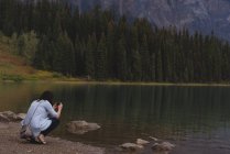 Vista trasera de la mujer haciendo clic en las fotos con la cámara cerca del lago - foto de stock