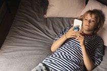 Donna che utilizza il telefono cellulare sul letto in camera da letto a casa — Foto stock