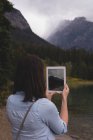 Rückansicht einer Frau, die Fotos mit einem digitalen Tablet am Seeufer anklickt — Stockfoto