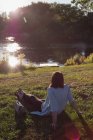 Задний вид на женщину, расслабляющуюся возле реки — стоковое фото