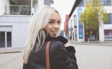Lächelnde blonde Frau blickt in die Kamera in der Stadt — Stockfoto