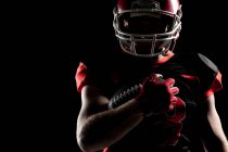 American Football-Spieler mit Helm hält Rugby-Ball vor schwarzem Hintergrund — Stockfoto