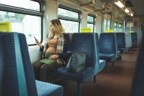 Belle femme enceinte utilisant un téléphone portable tout en voyageant en train — Photo de stock