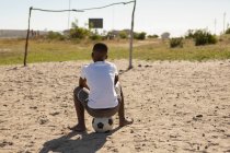 Visão traseira do menino sentado no futebol no chão — Fotografia de Stock