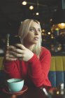 Жінка дивиться далеко під час використання мобільного телефону в кафе — стокове фото