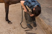 Woman putting horseshoes in horse leg at stable — Stock Photo