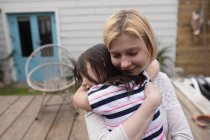 Мать обнимает свою дочь на заднем дворе дома — стоковое фото