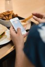 Крупним планом жінка, що їсть під час використання мобільного телефону в ресторані — стокове фото