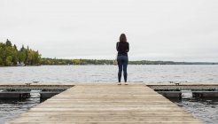 Вид сзади женщины, стоящей на пирсе возле реки — стоковое фото