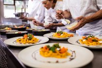 Chef garnishing food on plates in kitchen — Stock Photo