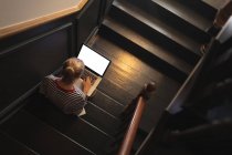 Накладные расходы женщины, использующей ноутбук на лестнице дома — стоковое фото
