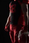 Seção média do jogador de futebol americano de pé com capacete contra fundo preto — Fotografia de Stock