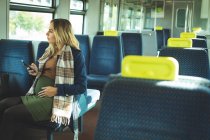 Беременная женщина смотрит в окно во время использования мобильного телефона в поезде — стоковое фото