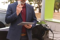 Sección media del hombre de negocios que usa la tableta digital mientras habla en el teléfono móvil - foto de stock