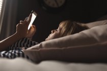 Frau benutzte Handy auf dem Bett im Schlafzimmer zu Hause — Stockfoto