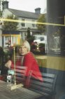 Mulher olhando através da janela enquanto mexendo café no café — Fotografia de Stock