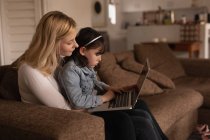 Madre e hija usando el ordenador portátil en la sala de estar en casa - foto de stock