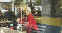Жінка дивиться крізь вікно, перемішуючи каву в кафе — стокове фото