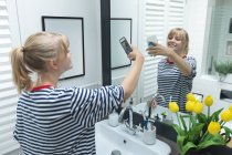 Женщина делает селфи на мобильный телефон в ванной комнате дома — стоковое фото