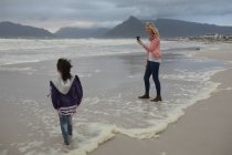 Felice madre cliccando foto di sua figlia in spiaggia — Foto stock