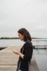 Женщина, использующая мобильный телефон на пирсе возле реки — стоковое фото