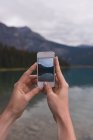 Primo piano della donna cliccando foto con il telefono cellulare vicino al lago — Foto stock
