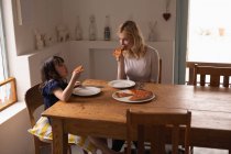 Mother and daughter having food on dining table at home — Stock Photo