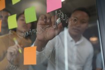 Männliche Führungskraft schreibt auf Glaswand im Büro — Stockfoto