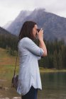 Seitenansicht einer Frau, die Fotos mit der Kamera am Seeufer anklickt — Stockfoto