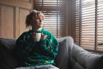 Женщина пьет кофе, сидя дома на диване — стоковое фото
