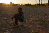 Хлопчик сидить на футболі в землі в сутінках — стокове фото