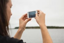 Крупним планом жінка натискає фотографії з мобільним телефоном біля берега річки — стокове фото